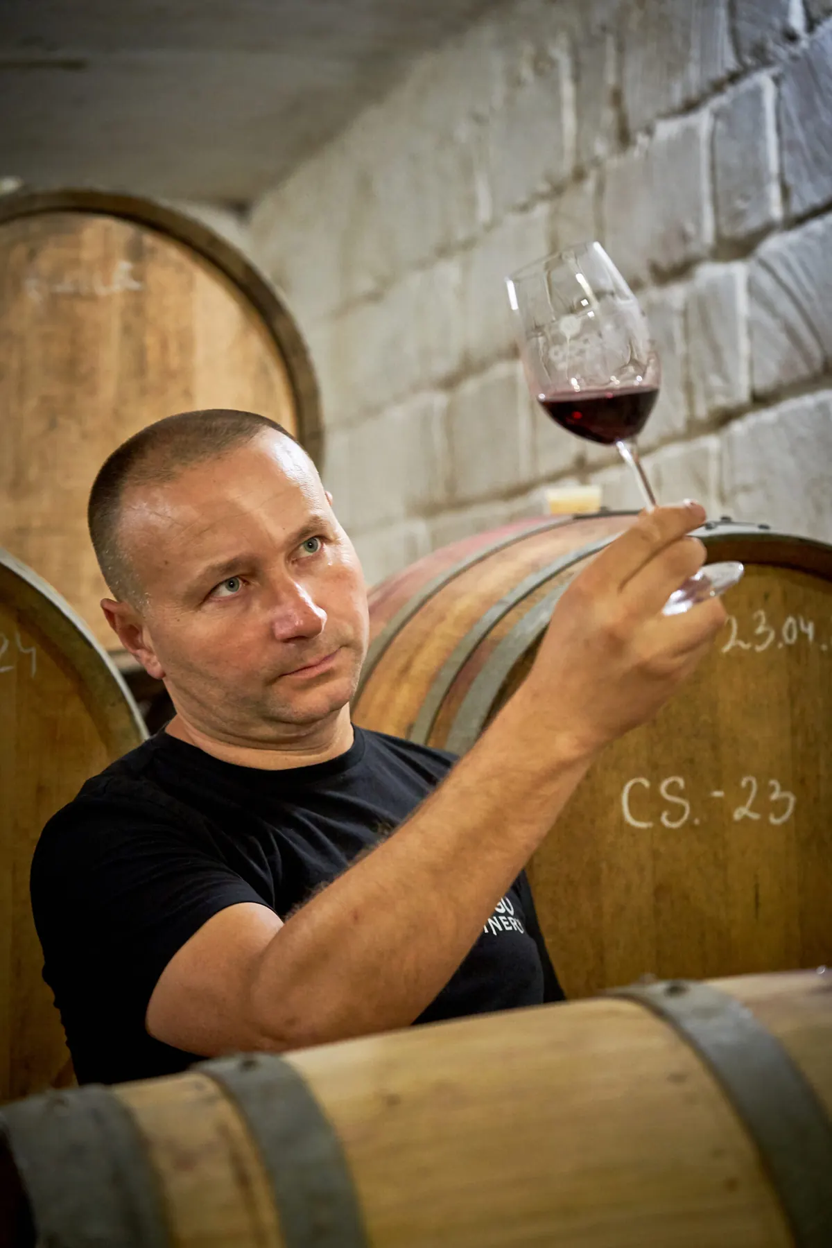 Ilie Gogu în pivniță, privind vinul în pahar lângă un butoi